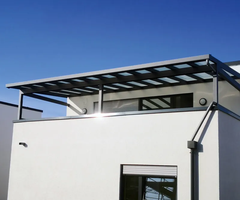 Balkonüberdachung mit flachem Pultdach und Glasfeldern an einem weißen Mehrfamilienhaus unter blauem Himmel
