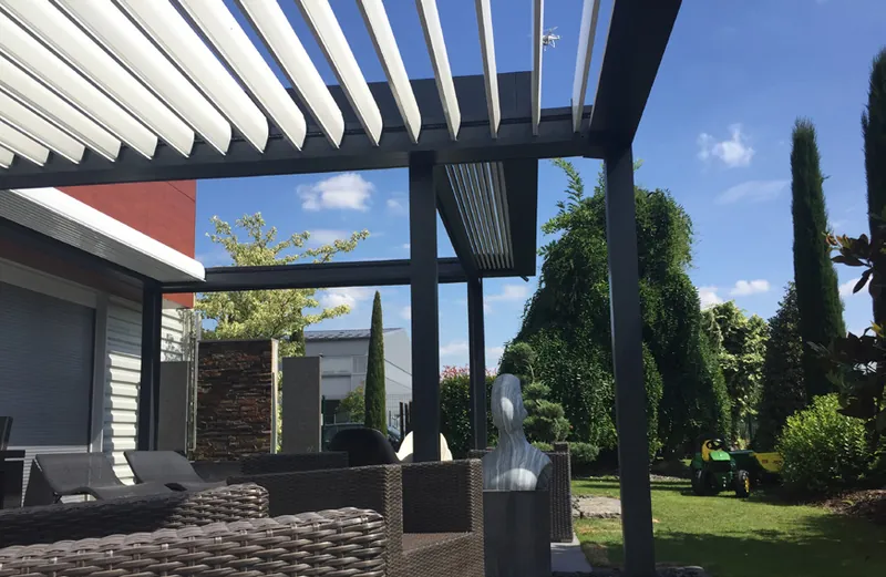 Lamellenüberdachung mit weißen, steil geöffneten Lamellen über einer Gartenlounge mit Rattansesseln