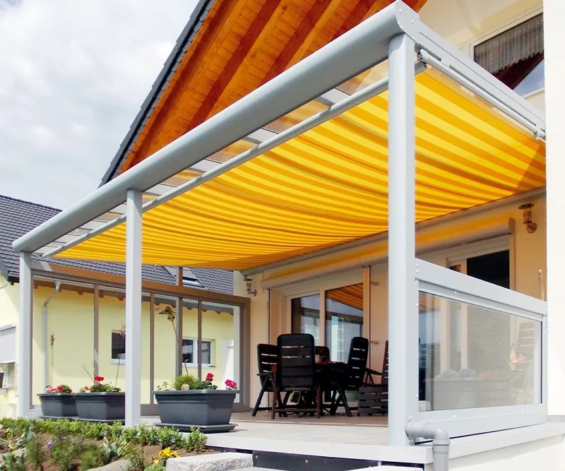 Gelb-weiß gestreifte Markise unter einem Terrassendach mit Glasbrüstung und Blumenkästen