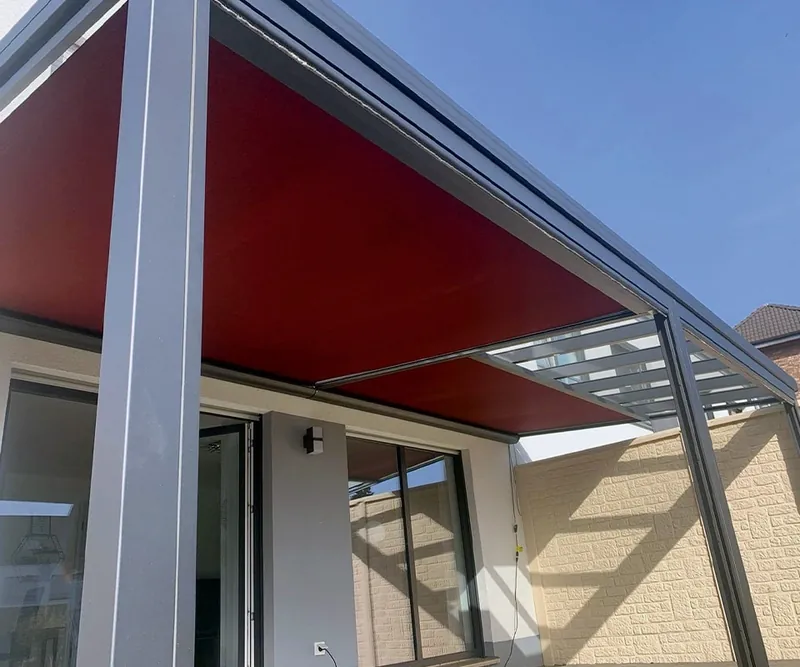 Rotbraune Markise unter einem Glasdach an einem Haus mit hellem Klinkersockel