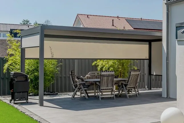Freistehende Überdachung mit beiger Senkrechtmarkise als Rückwand und Esstisch mit Holzstühlen