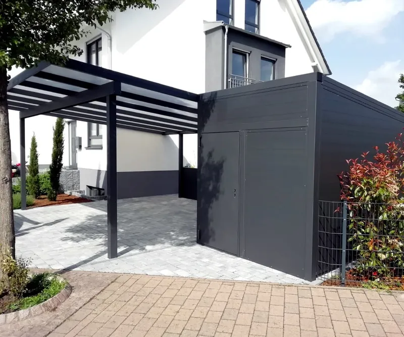 Anthrazitfarbenes Gerätehaus mit Tür neben einem Carport mit Pultdach vor einem Wohnhaus