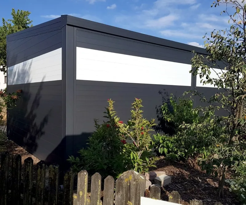 Gerätehaus in Anthrazit mit hellem Fensterband in einem Garten mit Zaun