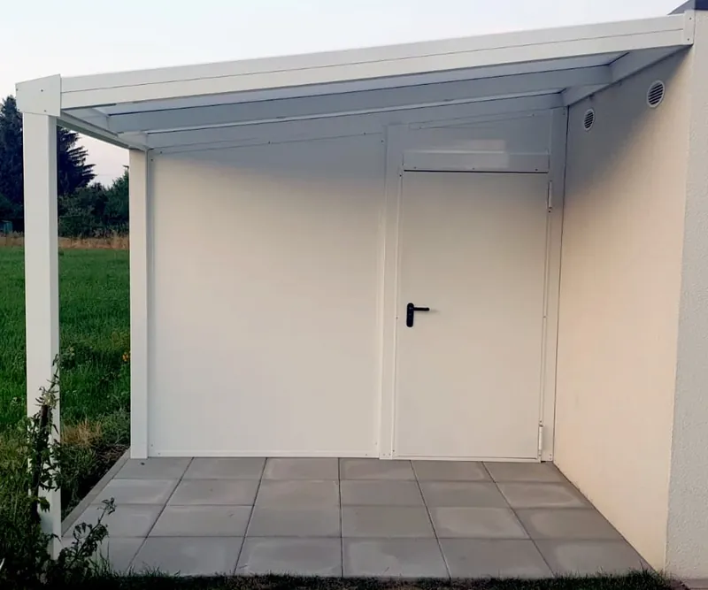 Weißes Gerätehaus unter einem überstehenden Pultdach mit Zweiflügeltür, Terrassenplatten davor